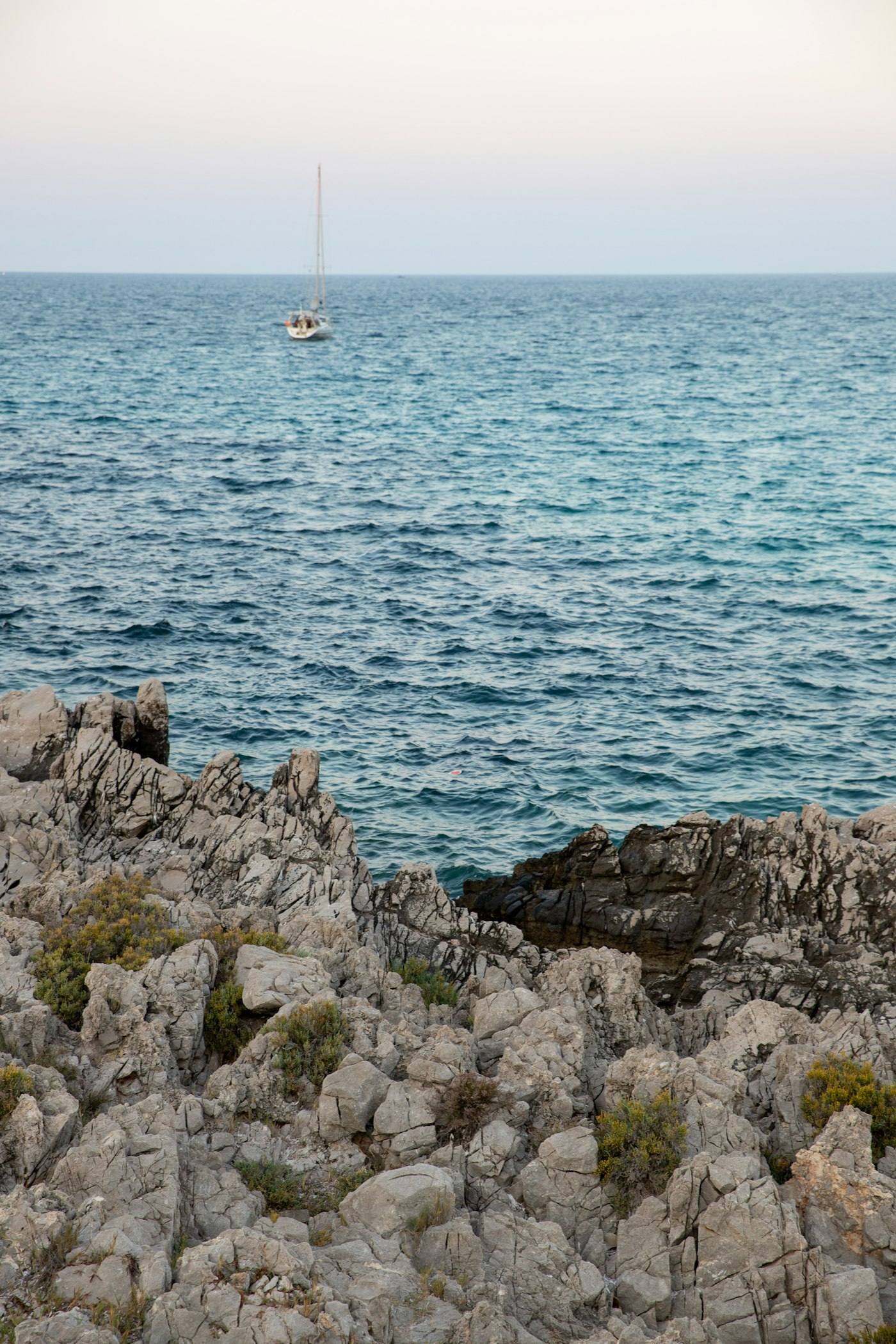 Sailboat on the Mediterranean beyond dark lava rocks