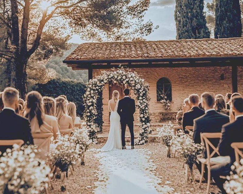 Outdoor wedding ceremony beside a rustic stone chapel